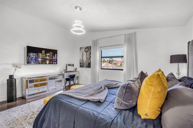 bedroom featuring hardwood / wood-style floors, lofted ceiling, a textured ceiling, and an inviting chandelier