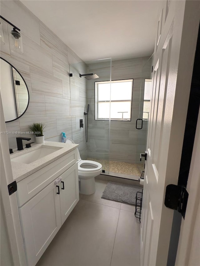 bathroom featuring vanity, a shower with door, tile walls, tile patterned flooring, and toilet