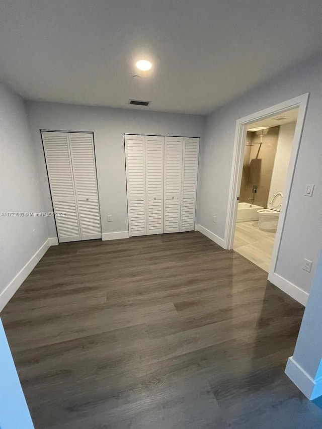 unfurnished bedroom featuring ensuite bathroom, dark wood-type flooring, and two closets