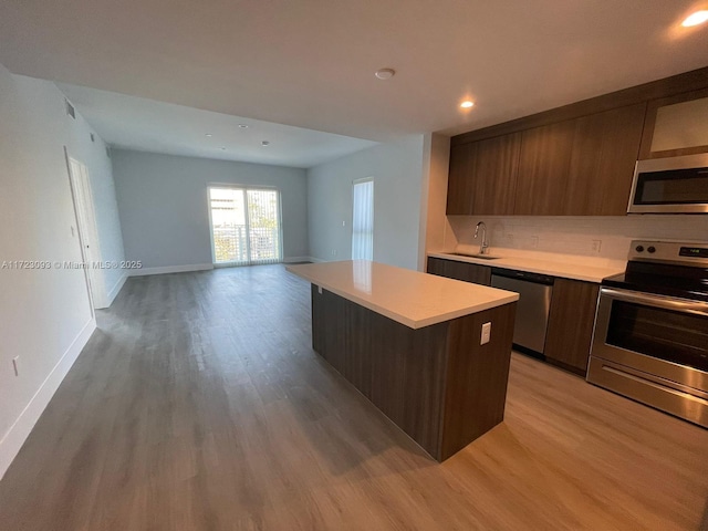 kitchen with a kitchen breakfast bar, light wood-type flooring, stainless steel appliances, sink, and a kitchen island