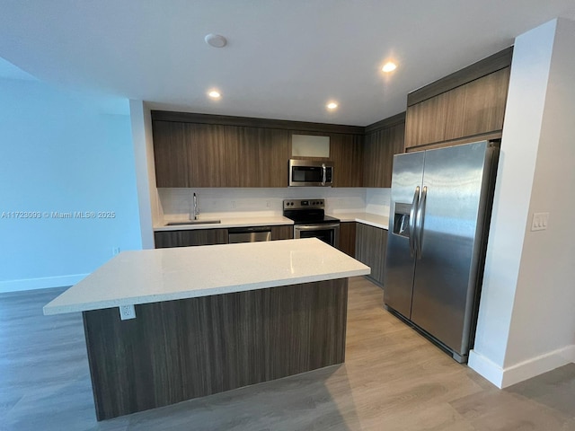 kitchen with dark brown cabinetry, stainless steel appliances, sink, light hardwood / wood-style flooring, and a kitchen island