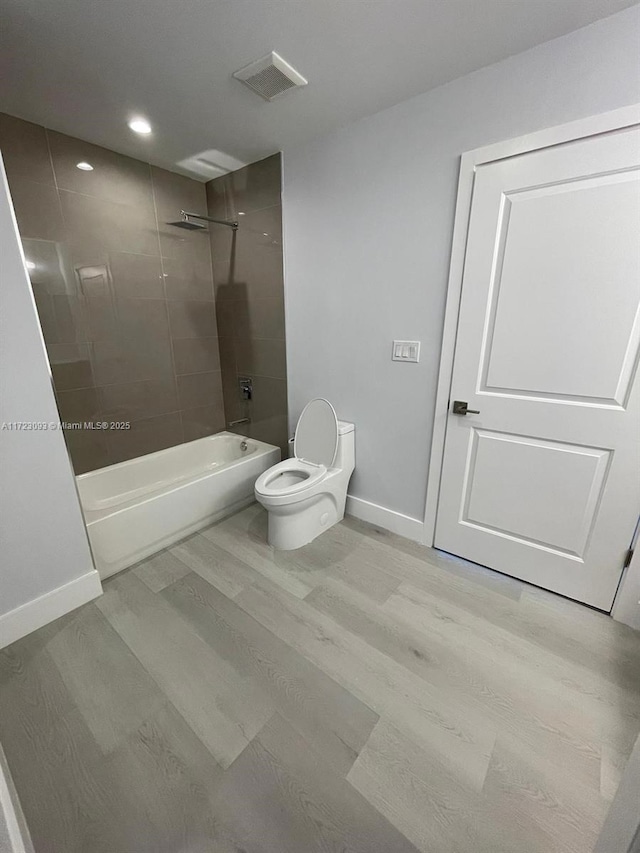 bathroom featuring hardwood / wood-style flooring, tiled shower / bath combo, and toilet