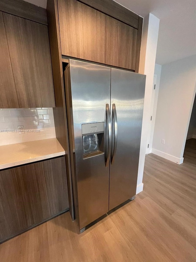 kitchen featuring stainless steel fridge, light hardwood / wood-style floors, and backsplash