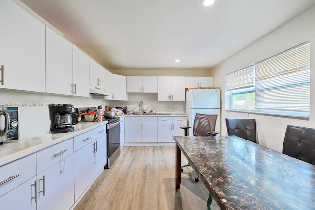 kitchen with a sink, light wood-style floors, range with electric cooktop, under cabinet range hood, and freestanding refrigerator