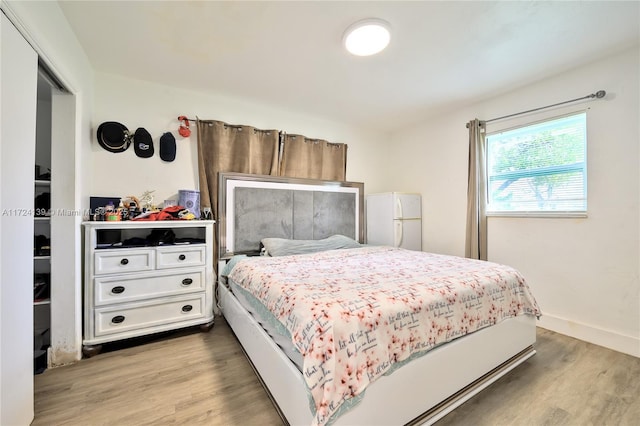 bedroom with baseboards, wood finished floors, and freestanding refrigerator