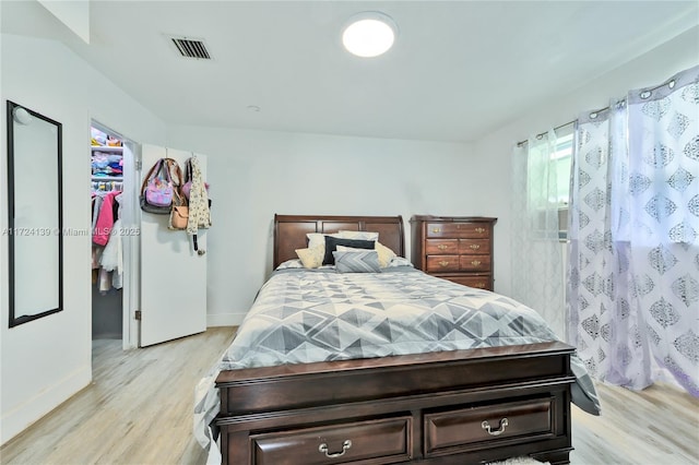 bedroom with visible vents, a walk in closet, light wood-type flooring, a closet, and baseboards