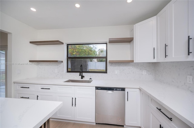 kitchen with light wood-type flooring, tasteful backsplash, stainless steel dishwasher, sink, and white cabinetry