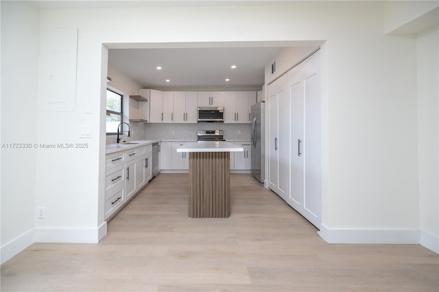 kitchen with decorative backsplash, a kitchen island, appliances with stainless steel finishes, light hardwood / wood-style floors, and white cabinetry