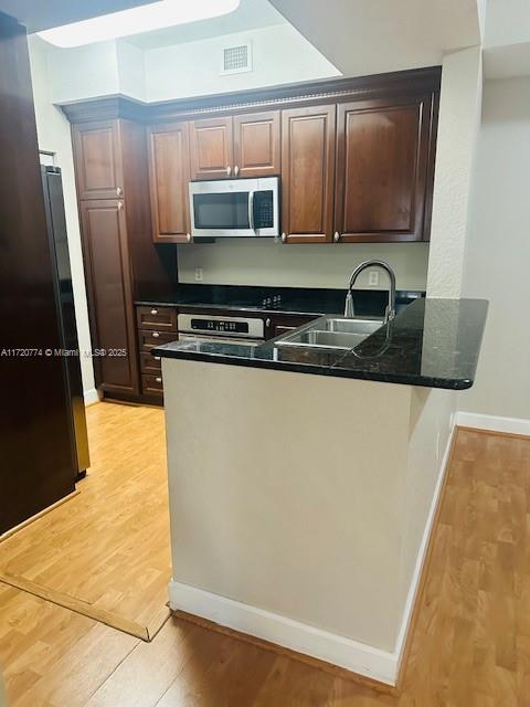 kitchen with sink, black fridge, kitchen peninsula, light wood-type flooring, and range