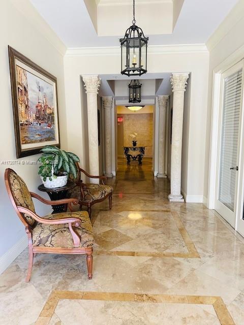 corridor featuring a raised ceiling, ornate columns, and ornamental molding