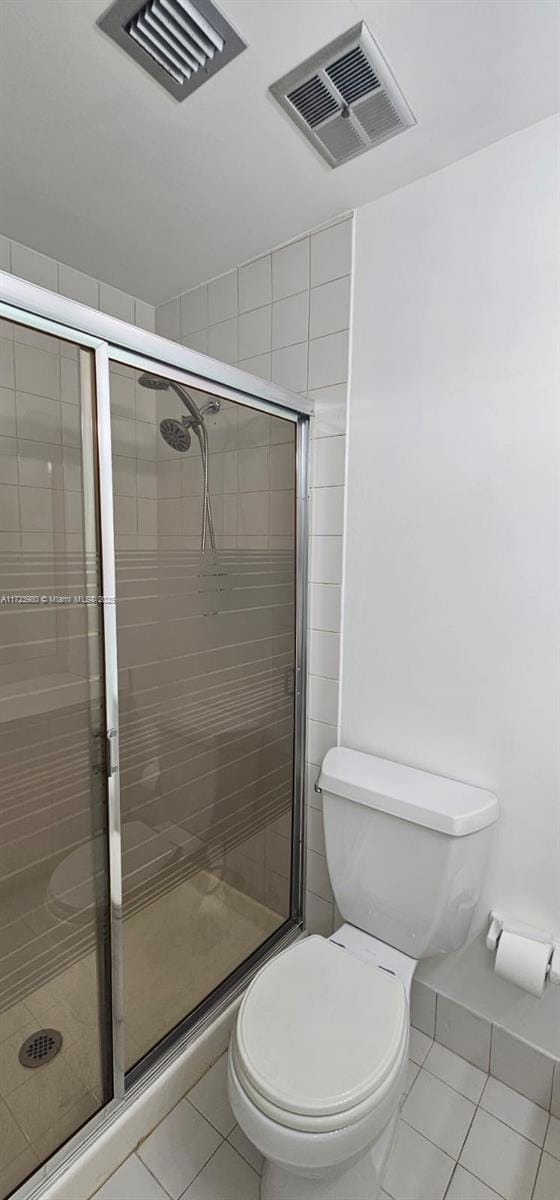 bathroom with tile patterned flooring, a shower with door, and toilet