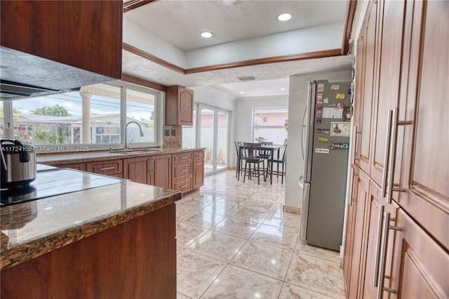 kitchen with cooktop, a textured ceiling, sink, dark stone countertops, and stainless steel refrigerator