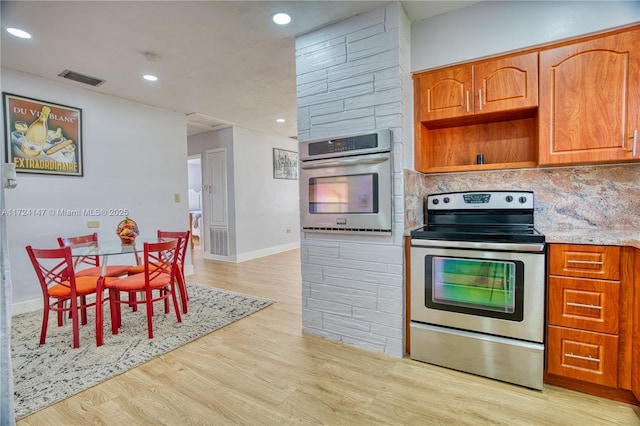 kitchen featuring backsplash, light stone counters, light wood-type flooring, and appliances with stainless steel finishes