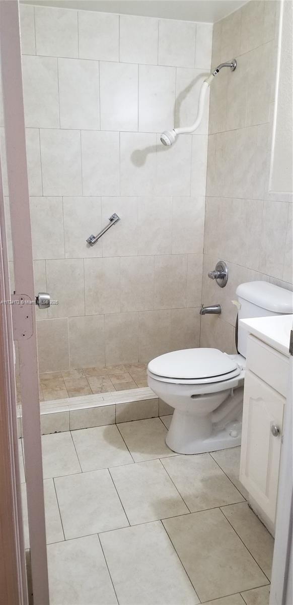 bathroom with toilet, tile patterned flooring, tiled shower, and vanity