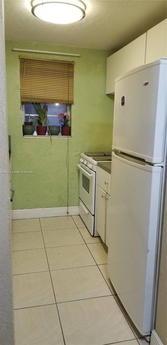 kitchen with white cabinets, light tile patterned flooring, and white appliances