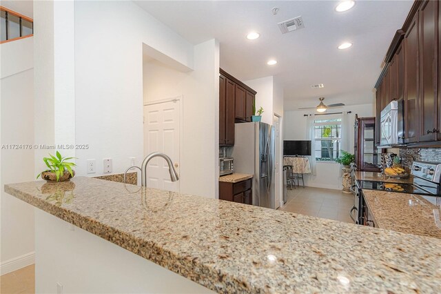 kitchen with light stone counters, kitchen peninsula, appliances with stainless steel finishes, ceiling fan, and dark brown cabinets