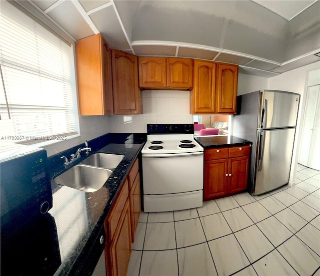 kitchen featuring white electric range, sink, dark stone countertops, light tile patterned flooring, and stainless steel refrigerator