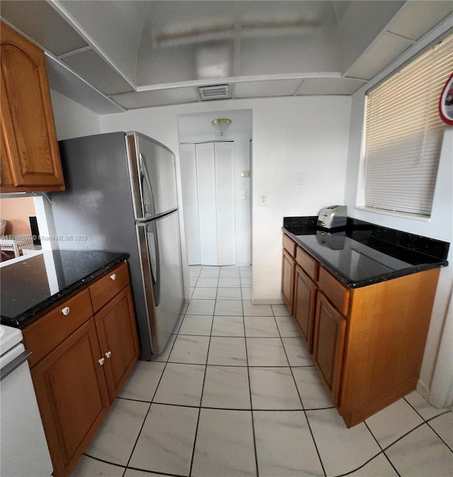 kitchen with light tile patterned floors, white stove, stainless steel refrigerator, and dark stone counters