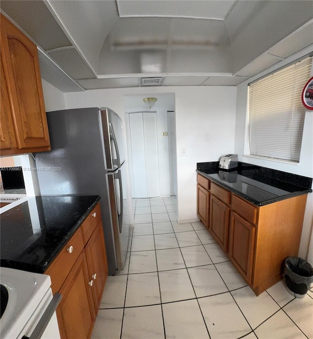 kitchen with stainless steel fridge, light tile patterned floors, and dark stone countertops