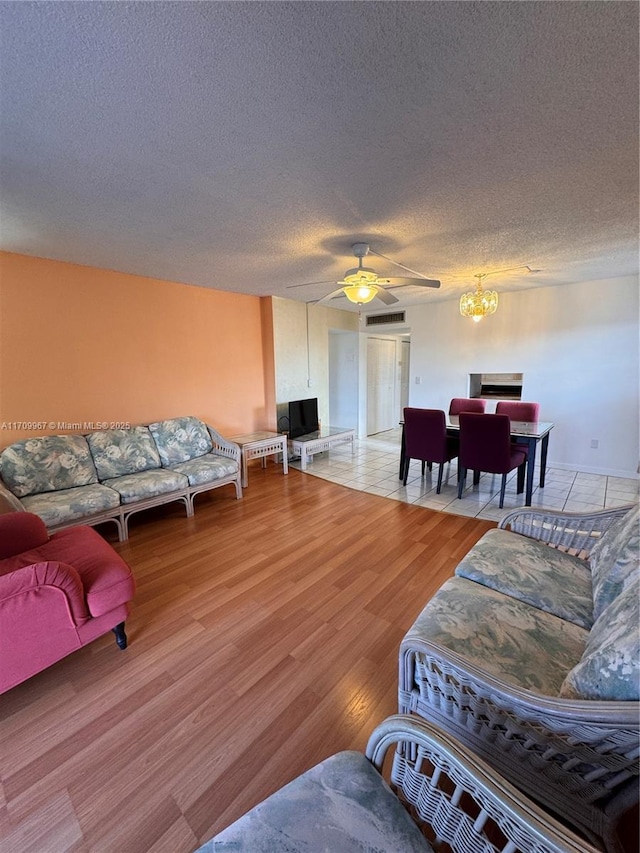 living room with a textured ceiling, ceiling fan with notable chandelier, and hardwood / wood-style flooring