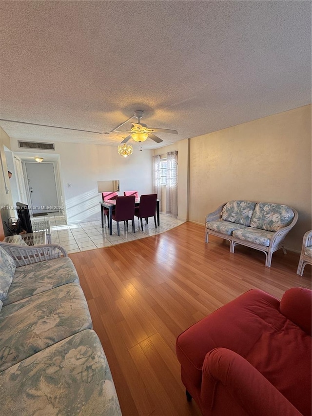 living room featuring ceiling fan, light hardwood / wood-style floors, and a textured ceiling