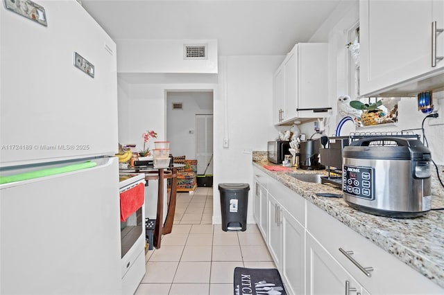 kitchen featuring white fridge, white cabinets, light stone countertops, and light tile patterned floors