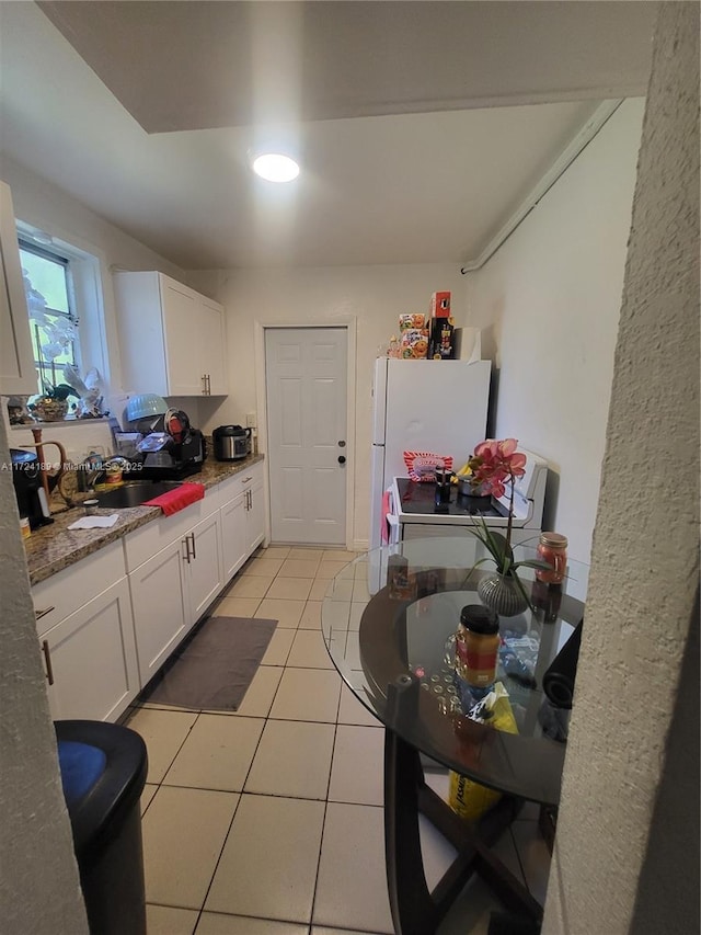 kitchen with sink, white cabinets, white fridge, light stone counters, and light tile patterned floors