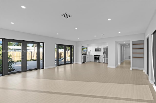 unfurnished living room featuring french doors, light hardwood / wood-style flooring, and sink