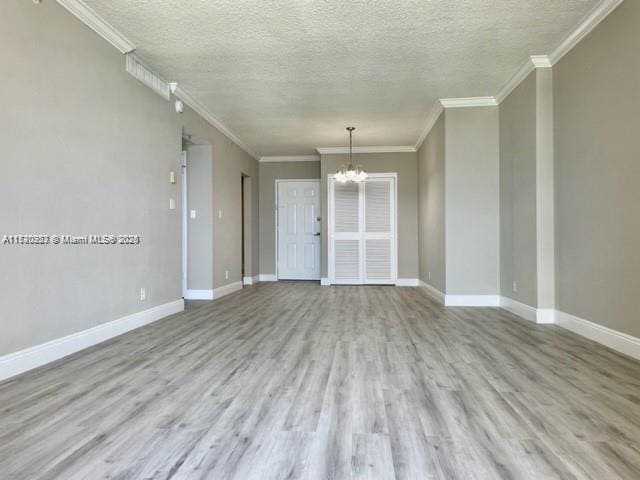 empty room with light hardwood / wood-style floors, ornamental molding, a textured ceiling, and a chandelier