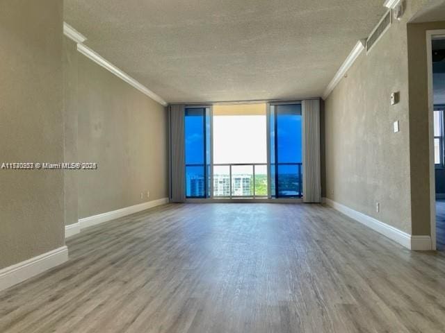 spare room featuring a textured ceiling, hardwood / wood-style flooring, floor to ceiling windows, and crown molding