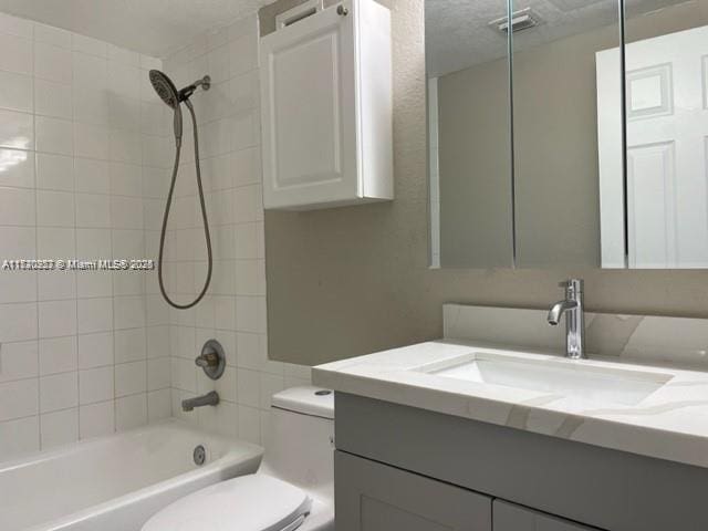 full bathroom featuring vanity, tiled shower / bath combo, and toilet