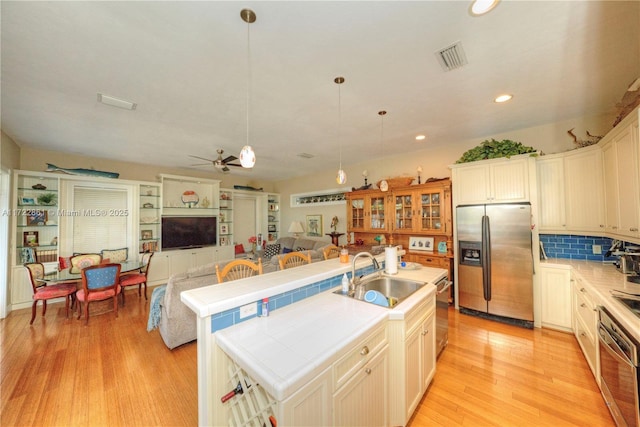 kitchen featuring an island with sink, ceiling fan, appliances with stainless steel finishes, pendant lighting, and sink