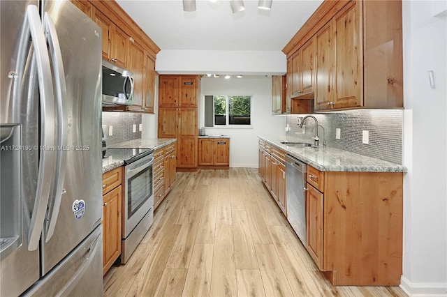 kitchen with sink, stainless steel appliances, light stone counters, tasteful backsplash, and light wood-type flooring