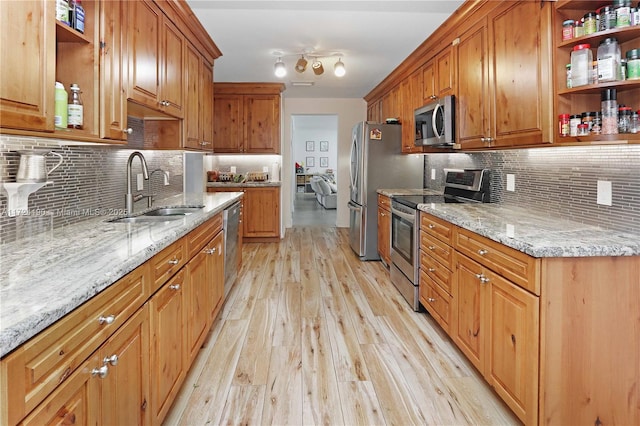 kitchen with sink, backsplash, stainless steel appliances, light hardwood / wood-style floors, and light stone countertops