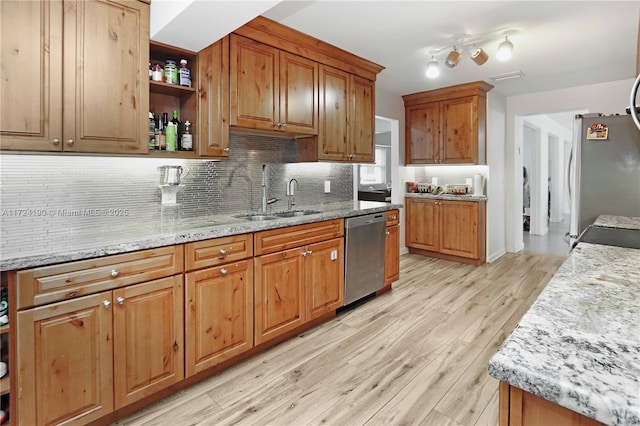 kitchen with sink, light stone counters, stainless steel appliances, light hardwood / wood-style floors, and decorative backsplash