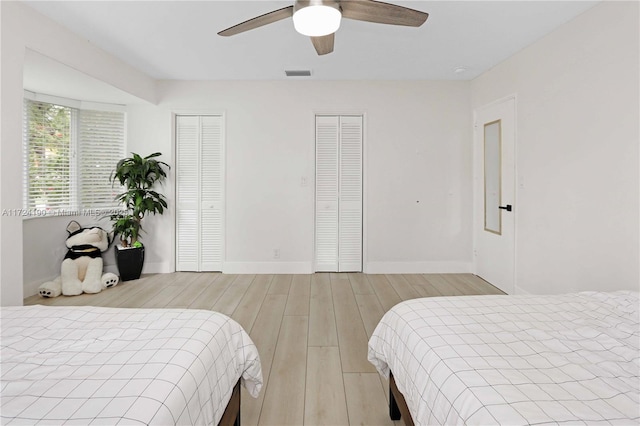 bedroom with multiple closets, ceiling fan, and light wood-type flooring