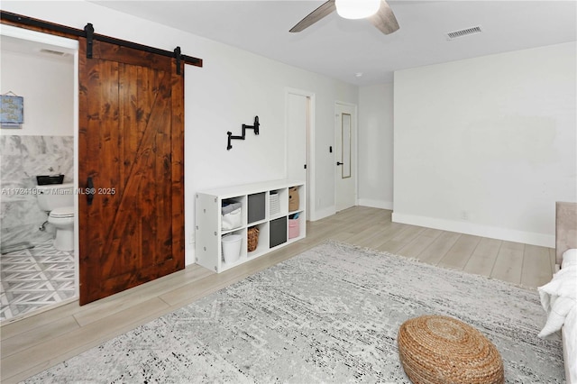 sitting room with a barn door, ceiling fan, and light wood-type flooring