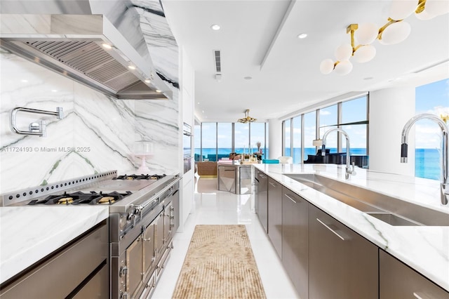 kitchen with sink, wall chimney range hood, stainless steel gas stovetop, backsplash, and a water view