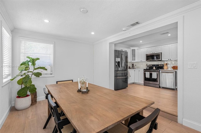 dining room with a textured ceiling, light wood-type flooring, and crown molding