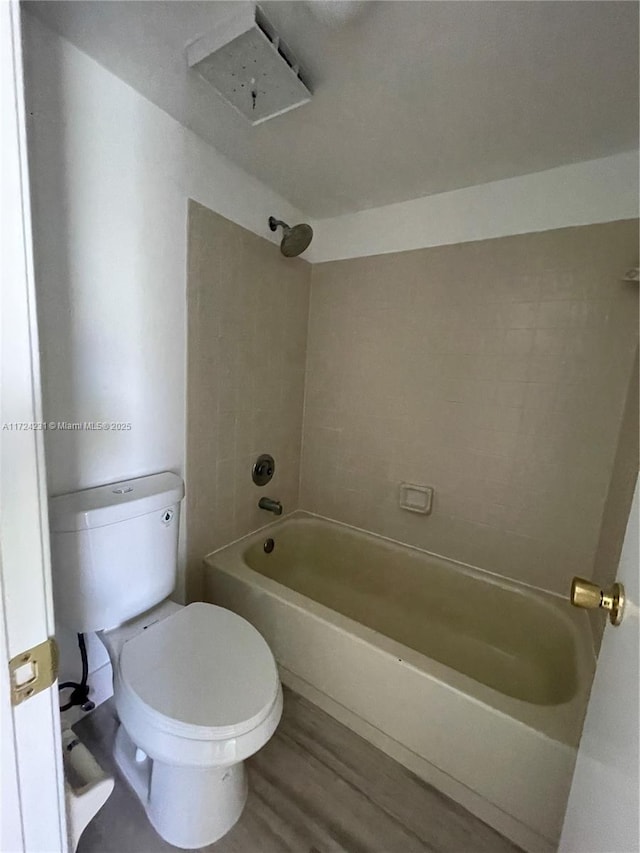 bathroom featuring wood-type flooring, tiled shower / bath combo, and toilet