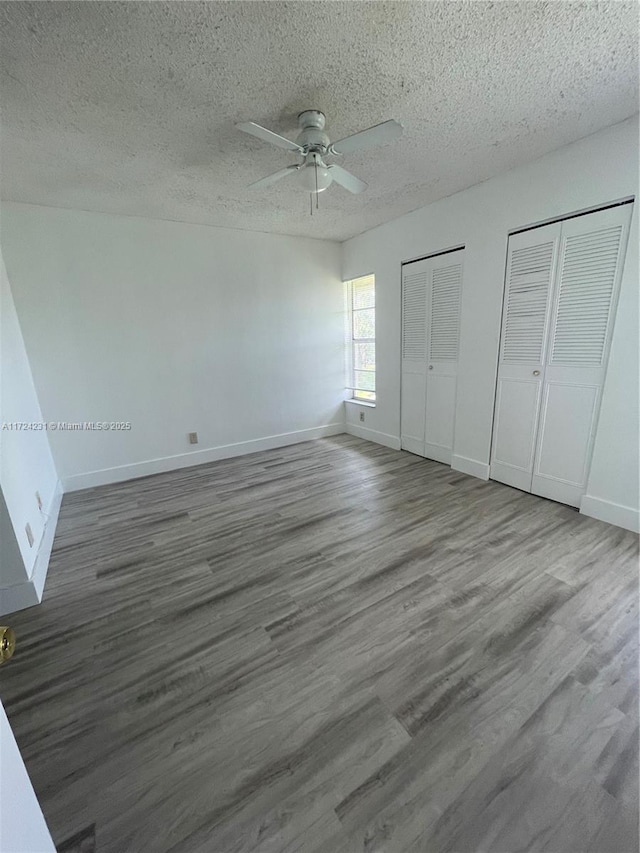 unfurnished bedroom featuring ceiling fan, wood-type flooring, a textured ceiling, and two closets