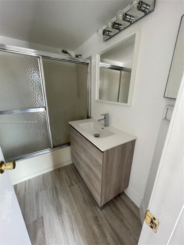 bathroom with hardwood / wood-style flooring, vanity, and shower / bath combination with glass door