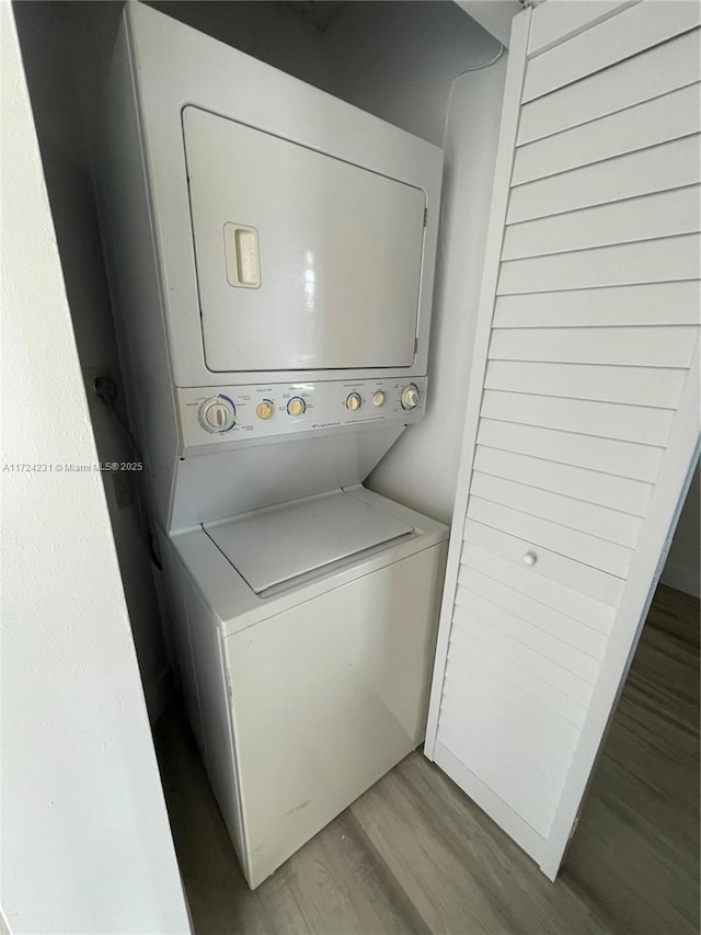 clothes washing area with hardwood / wood-style floors and stacked washer / drying machine