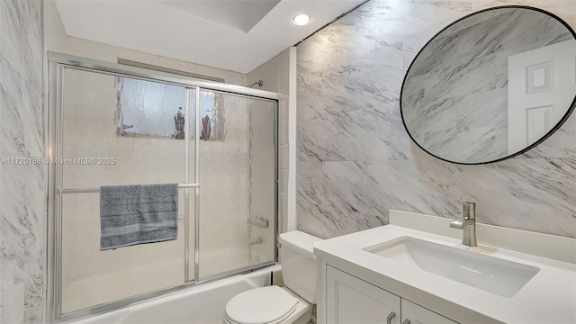 full bathroom with shower / bath combination with glass door, vanity, toilet, and tile walls