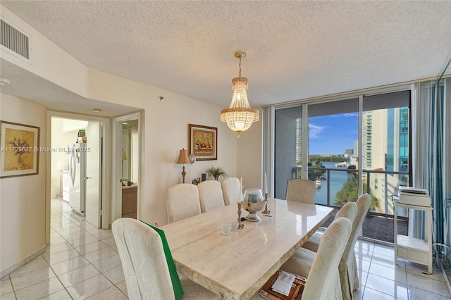 tiled dining area featuring a water view, an inviting chandelier, floor to ceiling windows, and a textured ceiling