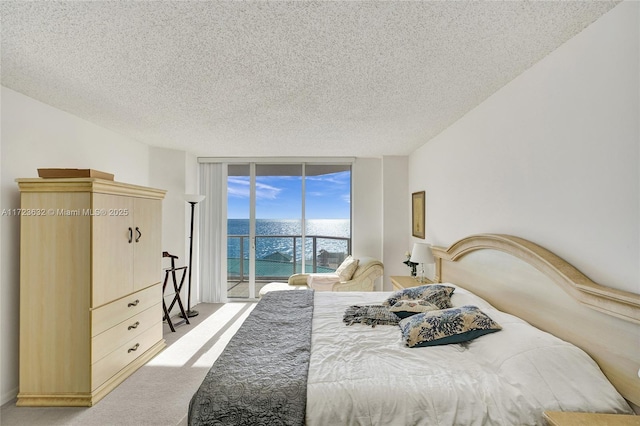 bedroom featuring a textured ceiling, access to exterior, a water view, floor to ceiling windows, and light colored carpet