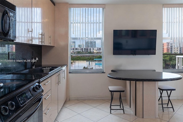 kitchen with light tile patterned floors, a kitchen bar, a healthy amount of sunlight, and black appliances