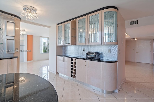 kitchen with decorative backsplash, an inviting chandelier, dark stone countertops, and light tile patterned floors