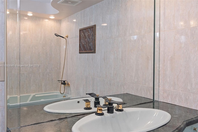 bathroom with tile walls, tiled shower / bath combo, and sink