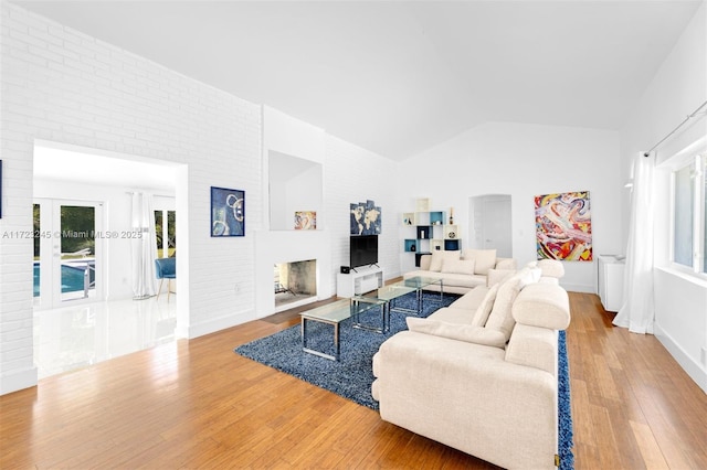 living room with hardwood / wood-style flooring, brick wall, and vaulted ceiling